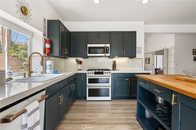 kitchen with decorative backsplash, appliances with stainless steel finishes, sink, butcher block countertops, and light hardwood / wood-style floors