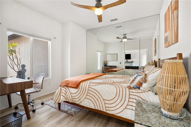 bedroom with ceiling fan, a fireplace, and light wood-type flooring