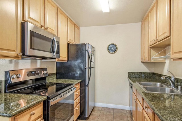 kitchen with light brown cabinets, light tile patterned floors, sink, stainless steel appliances, and dark stone countertops