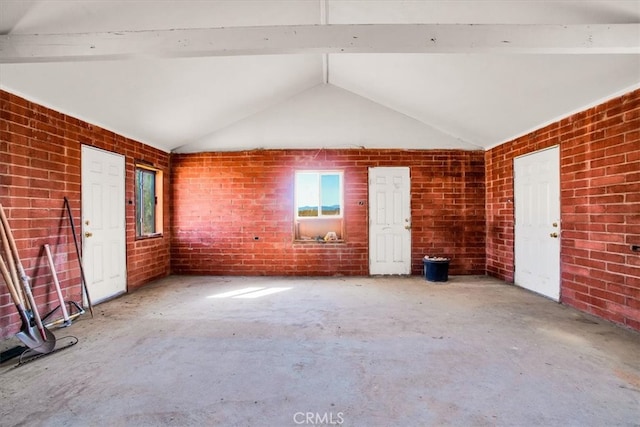 unfurnished living room with vaulted ceiling with beams, concrete flooring, and brick wall