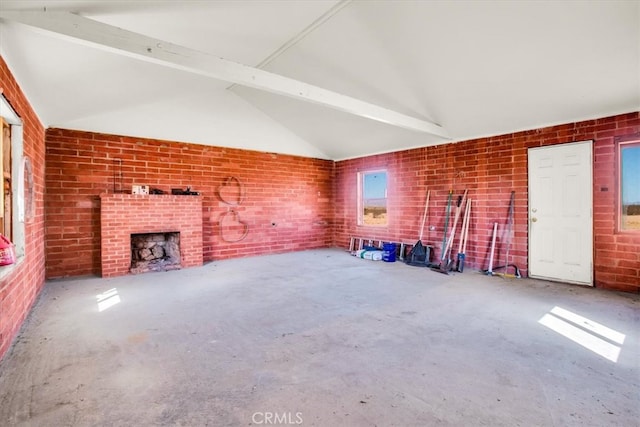 unfurnished living room with a brick fireplace, vaulted ceiling with beams, brick wall, and concrete floors