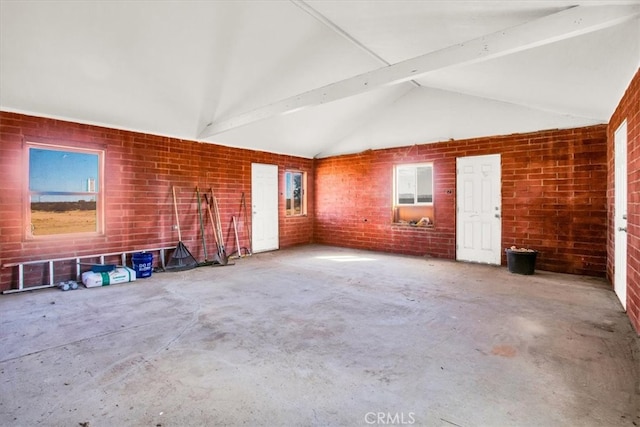 unfurnished living room featuring lofted ceiling with beams, concrete flooring, and brick wall