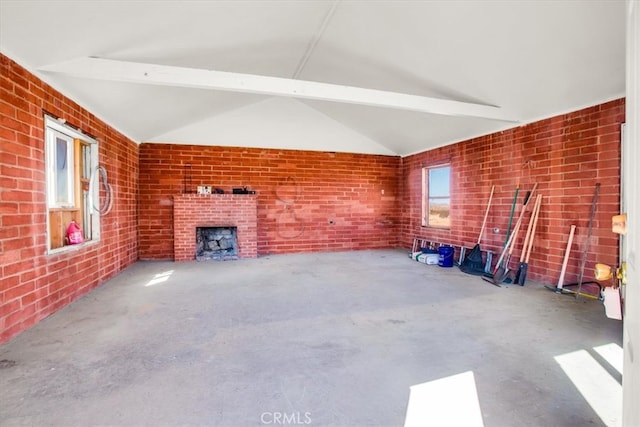 unfurnished living room with brick wall, vaulted ceiling with beams, a fireplace, and concrete flooring