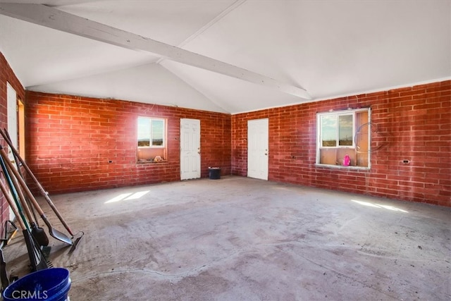 empty room featuring brick wall and lofted ceiling with beams