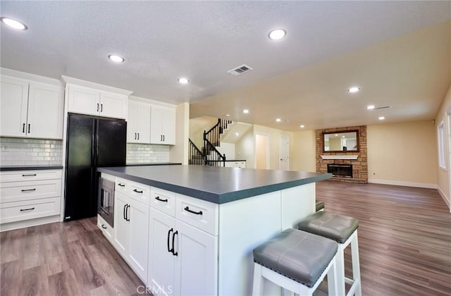 kitchen featuring white cabinetry, black fridge, dark hardwood / wood-style floors, and a stone fireplace