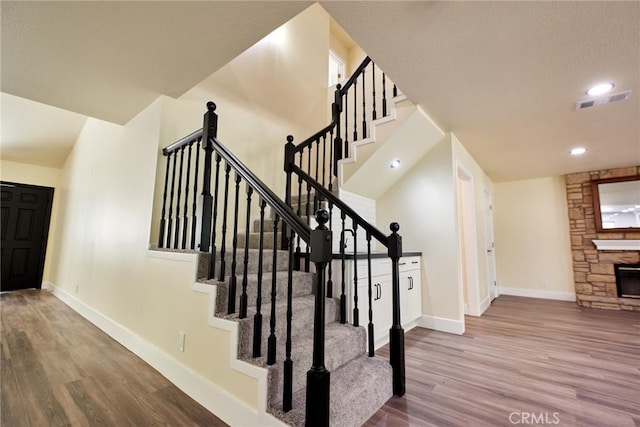 stairway featuring hardwood / wood-style floors and a stone fireplace