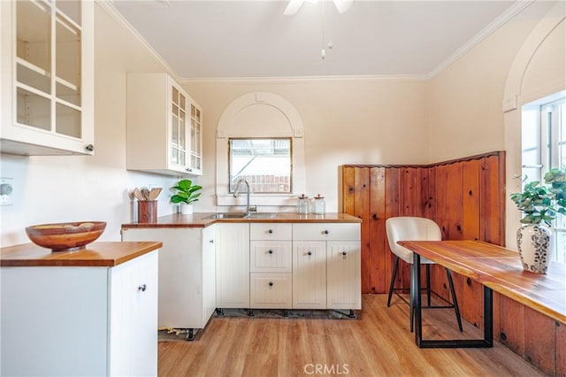 kitchen featuring wood counters, sink, crown molding, light hardwood / wood-style flooring, and white cabinets