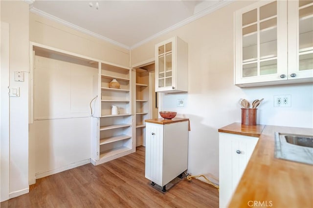 kitchen with butcher block countertops, light hardwood / wood-style flooring, ornamental molding, and white cabinets