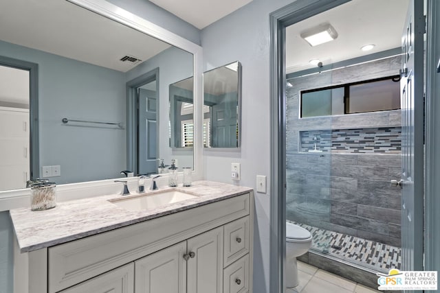 bathroom featuring toilet, vanity, tiled shower, and tile patterned flooring