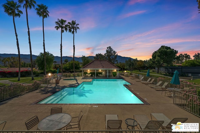 pool at dusk featuring a mountain view and a patio