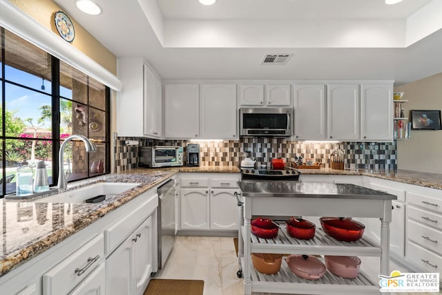 kitchen featuring sink, backsplash, white cabinetry, light stone countertops, and stainless steel appliances