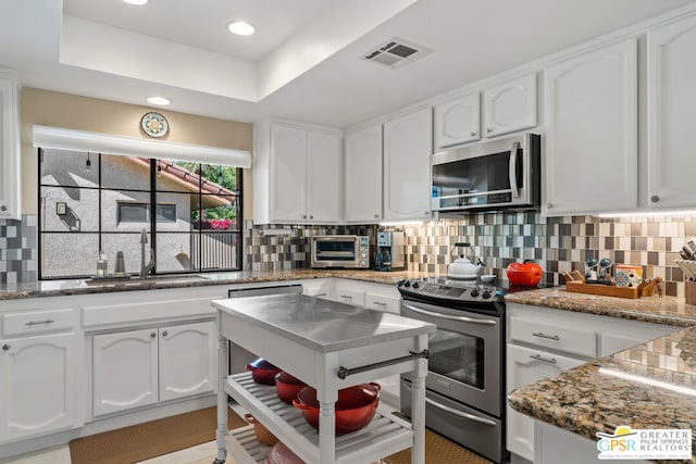 kitchen with a raised ceiling, sink, white cabinets, decorative backsplash, and stainless steel appliances