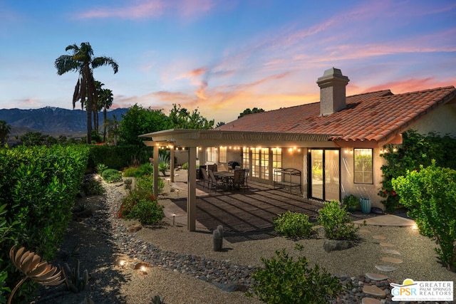 back house at dusk with a mountain view and a patio