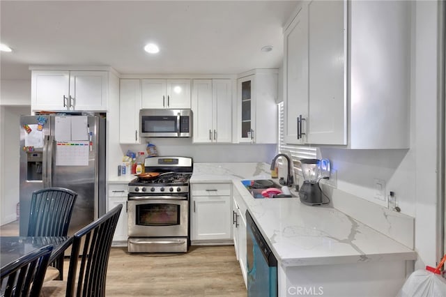 kitchen featuring light stone counters, stainless steel appliances, sink, light hardwood / wood-style floors, and white cabinetry