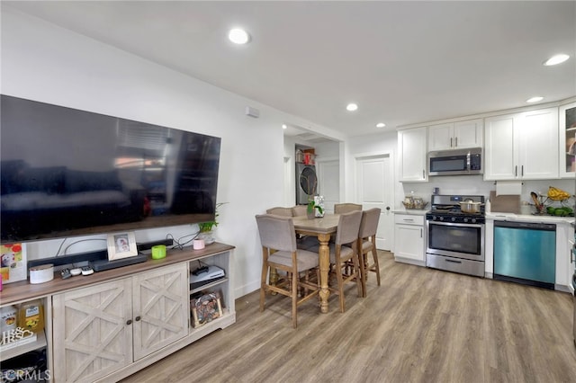 kitchen with stacked washing maching and dryer, white cabinets, light wood-type flooring, and appliances with stainless steel finishes