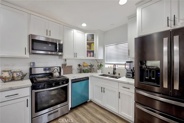 kitchen with sink, stainless steel appliances, light stone counters, white cabinets, and light wood-type flooring