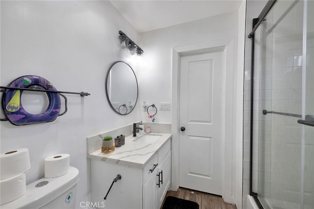 bathroom featuring wood-type flooring, vanity, toilet, and a shower with shower door