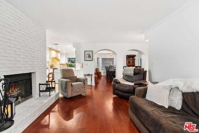 living room with wood-type flooring, ornamental molding, and a brick fireplace