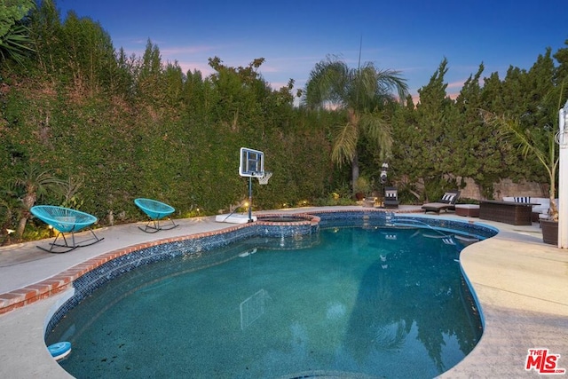 pool at dusk with a patio and an in ground hot tub