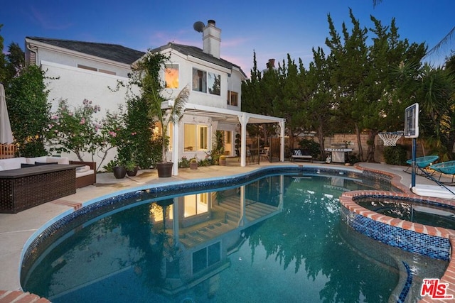 pool at dusk with a patio and an in ground hot tub