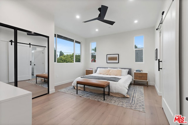 bedroom with ceiling fan, a barn door, multiple windows, and light hardwood / wood-style flooring