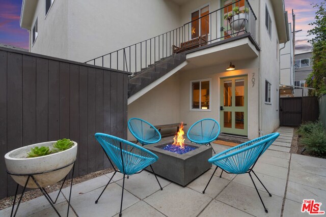 patio terrace at dusk featuring french doors, a balcony, and a fire pit