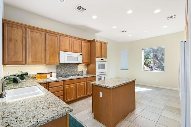 kitchen with a kitchen island, sink, white appliances, light tile patterned floors, and light stone counters