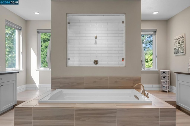 bathroom with vanity, a relaxing tiled tub, and plenty of natural light