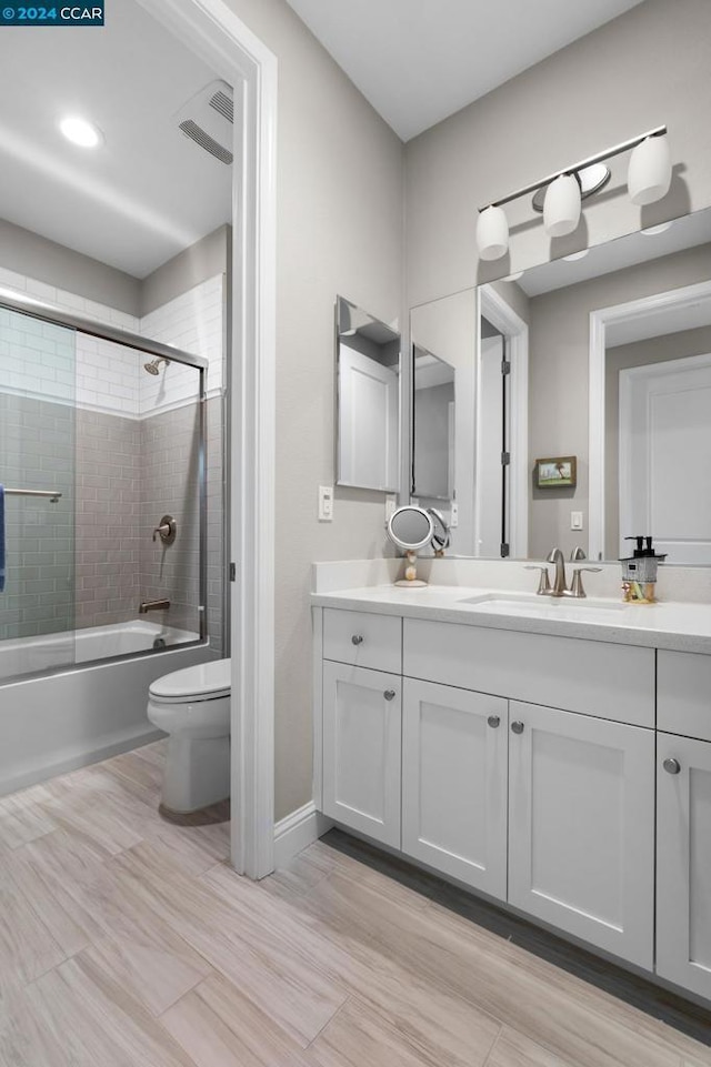 full bathroom with vanity, bath / shower combo with glass door, and toilet