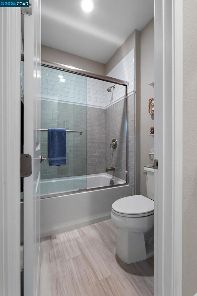 bathroom featuring toilet and shower / bath combination with glass door