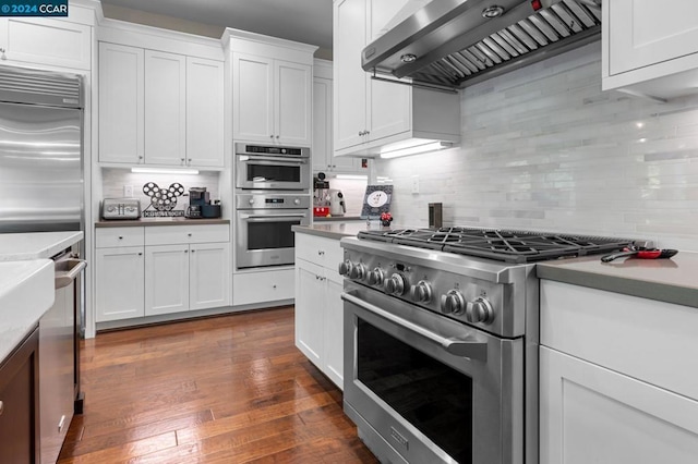 kitchen featuring white cabinets, wall chimney exhaust hood, tasteful backsplash, premium appliances, and dark hardwood / wood-style flooring