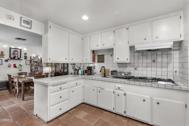 kitchen featuring white cabinetry, kitchen peninsula, tile counters, backsplash, and stainless steel gas cooktop