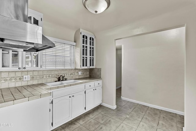 kitchen with tile countertops, island range hood, tasteful backsplash, white cabinets, and sink