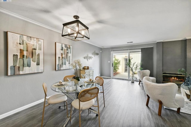 dining room featuring a large fireplace, crown molding, dark hardwood / wood-style flooring, and a chandelier