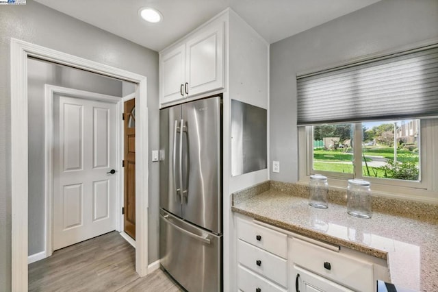 kitchen with light stone countertops, stainless steel fridge, light hardwood / wood-style floors, and white cabinetry