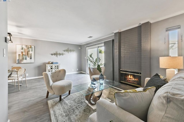 living room with crown molding, wood-type flooring, and a brick fireplace