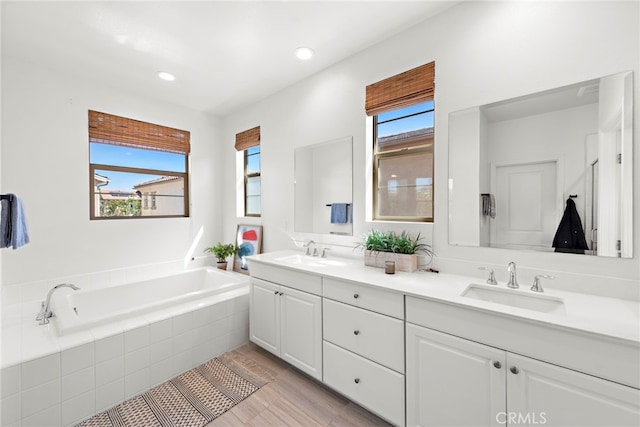 bathroom with tiled bath, plenty of natural light, and vanity