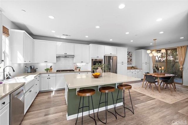 kitchen featuring pendant lighting, a center island, stainless steel appliances, sink, and light wood-type flooring