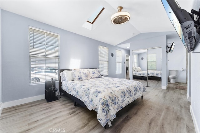 bedroom with ceiling fan, vaulted ceiling with skylight, a closet, light wood-type flooring, and ensuite bath