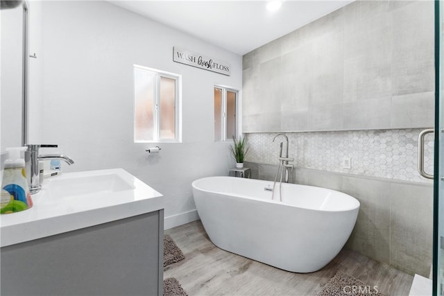 bathroom featuring tile walls, wood-type flooring, a tub, and vanity