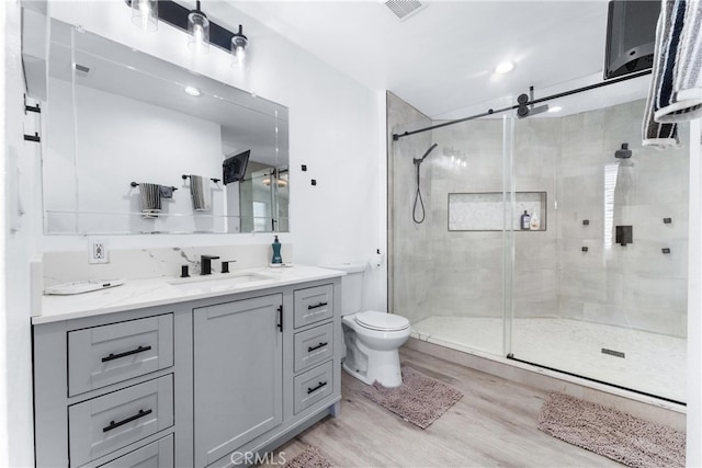 bathroom with a shower with door, hardwood / wood-style flooring, vanity, and toilet