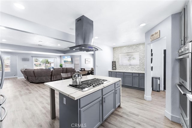 kitchen with gray cabinetry, a kitchen island, stainless steel gas cooktop, island exhaust hood, and light hardwood / wood-style flooring