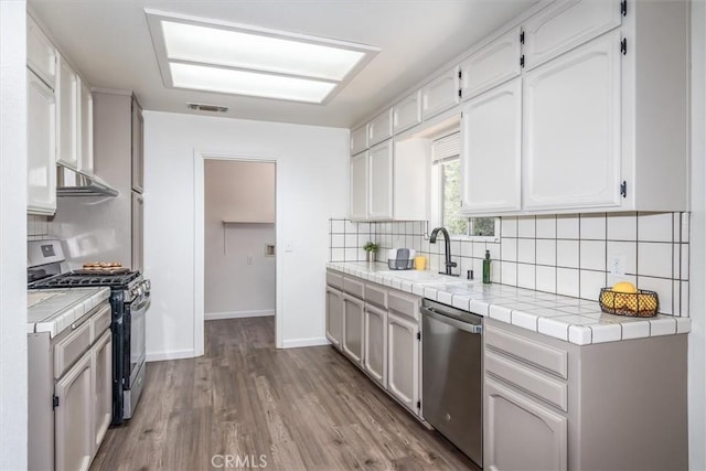 kitchen featuring tile countertops, white cabinets, sink, and appliances with stainless steel finishes