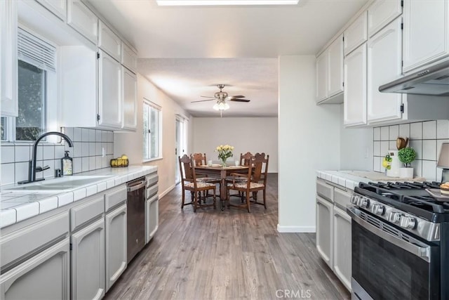 kitchen with backsplash, sink, tile counters, white cabinetry, and stainless steel appliances