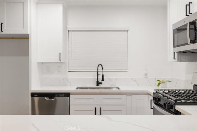 kitchen featuring white cabinetry, light stone counters, stainless steel appliances, and a sink