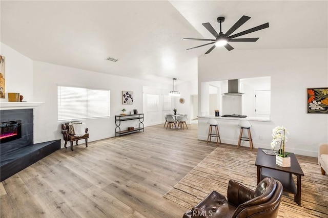 living area featuring ceiling fan, wood finished floors, visible vents, vaulted ceiling, and a glass covered fireplace