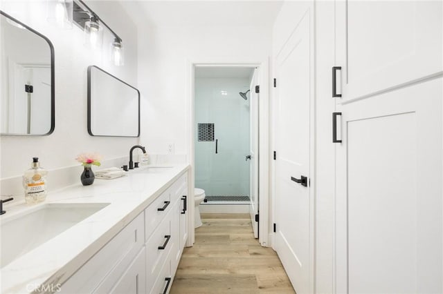 bathroom with double vanity, a sink, a shower stall, and wood finished floors