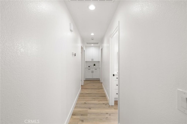 hallway featuring light wood-style floors, baseboards, and recessed lighting