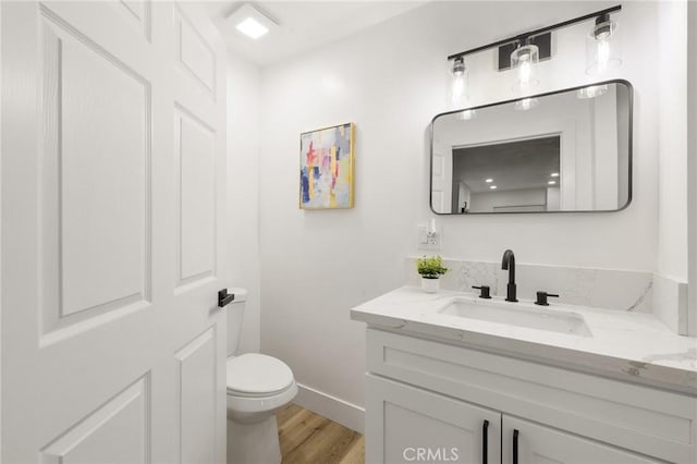 half bath with wood finished floors, vanity, toilet, and baseboards