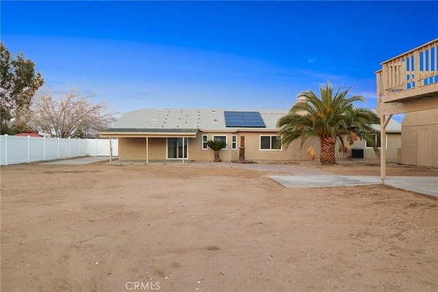 back of property featuring roof mounted solar panels and fence